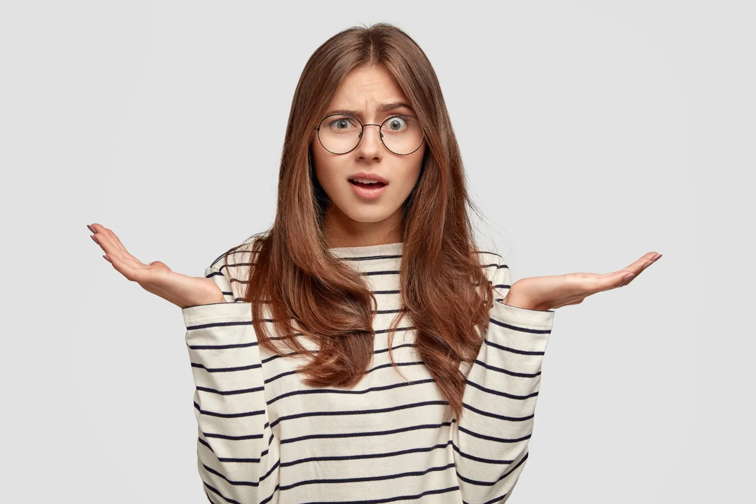 Femme devant un fond clair, les mains ouvertes dans un geste de questionnement.