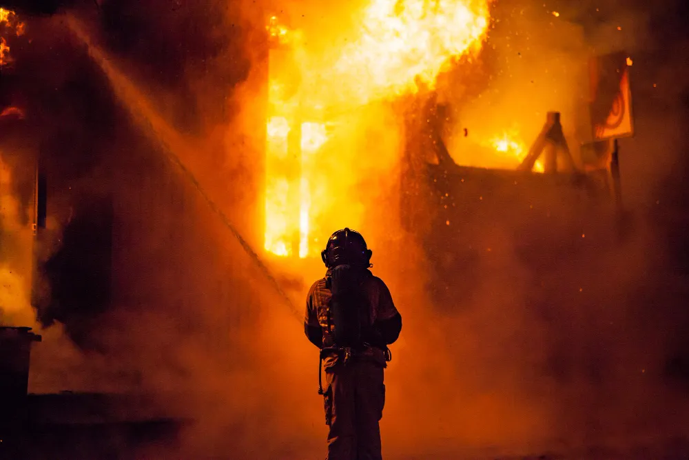 Pompier devant un bâtiment en flammes, illustrant l’importance des sorties d’urgence.