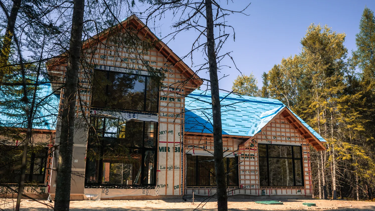 Maison en construction avec de grandes ouvertures vitrées donnant sur les arbres.
