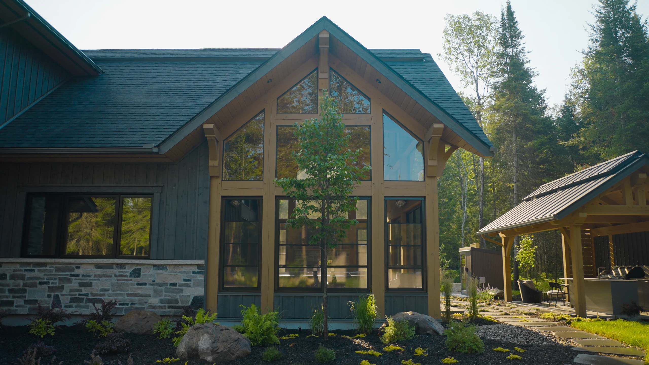 Façade d’un chalet avec grandes fenêtres sous un pignon et parement en pierre.