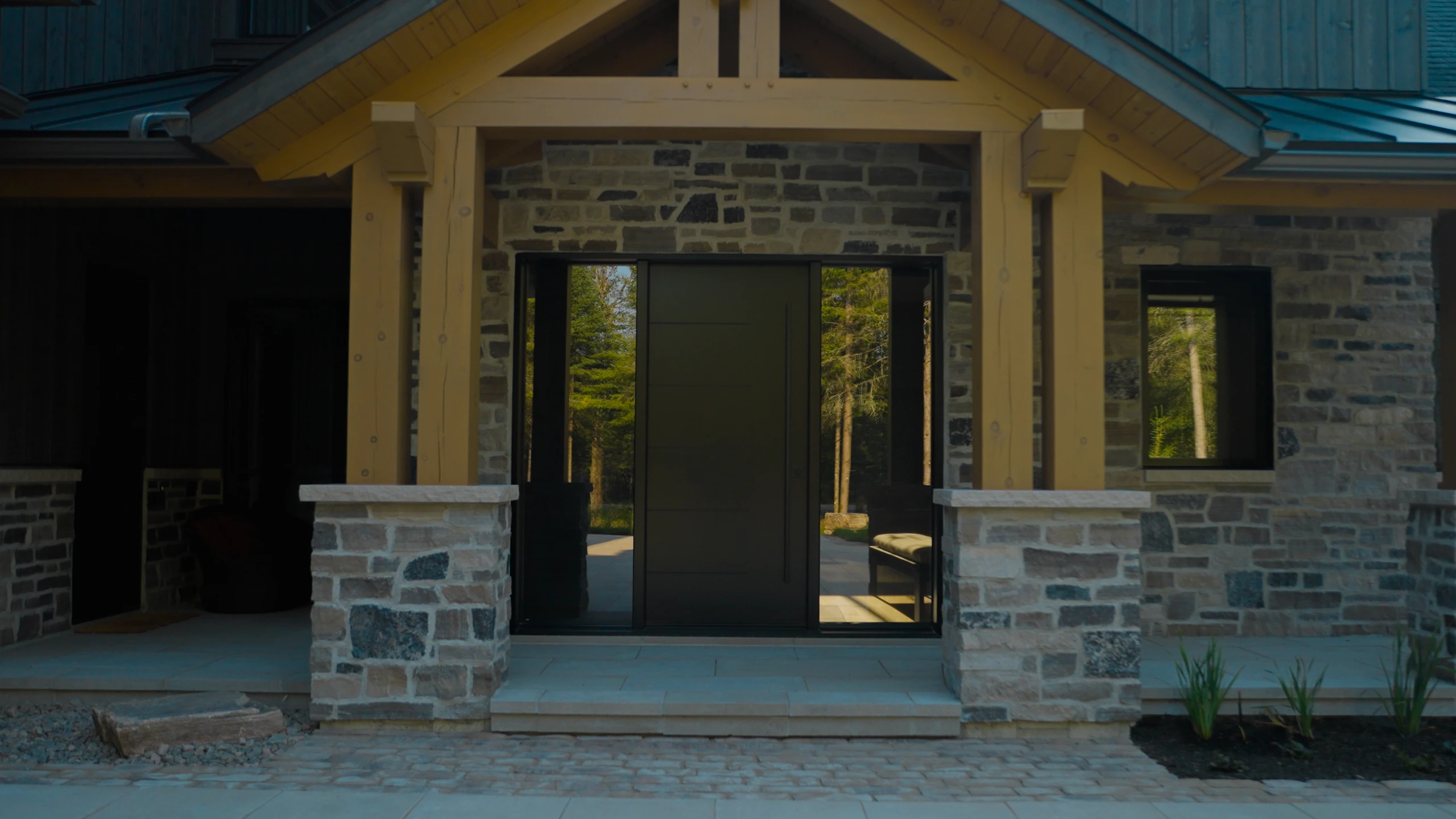 Porte d’entrée vitrée d’un chalet sous un porche en bois, entourée de pierre.
