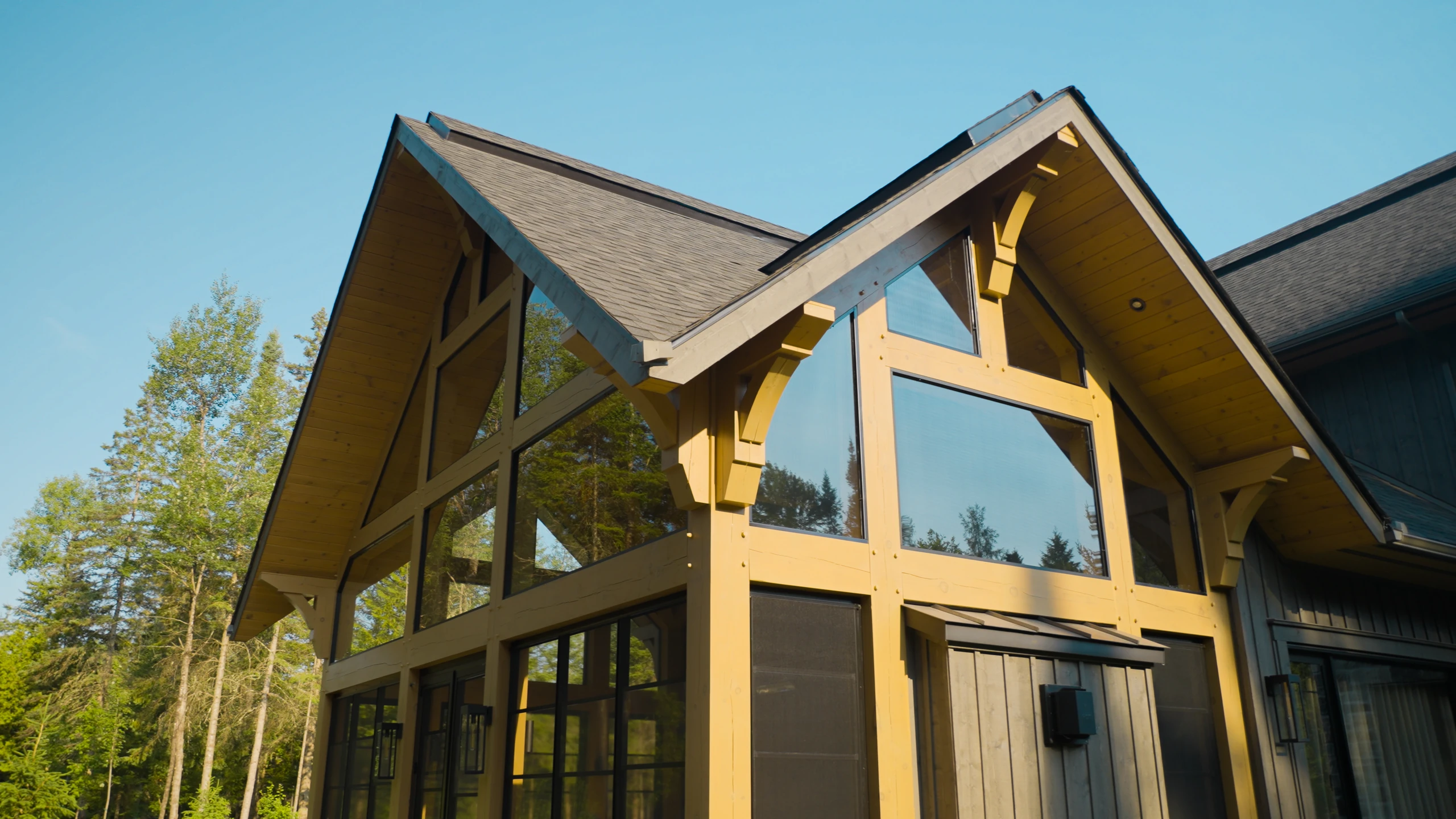 Façade à pignon d’un chalet avec fenêtres triangulaires et grandes baies vitrées.