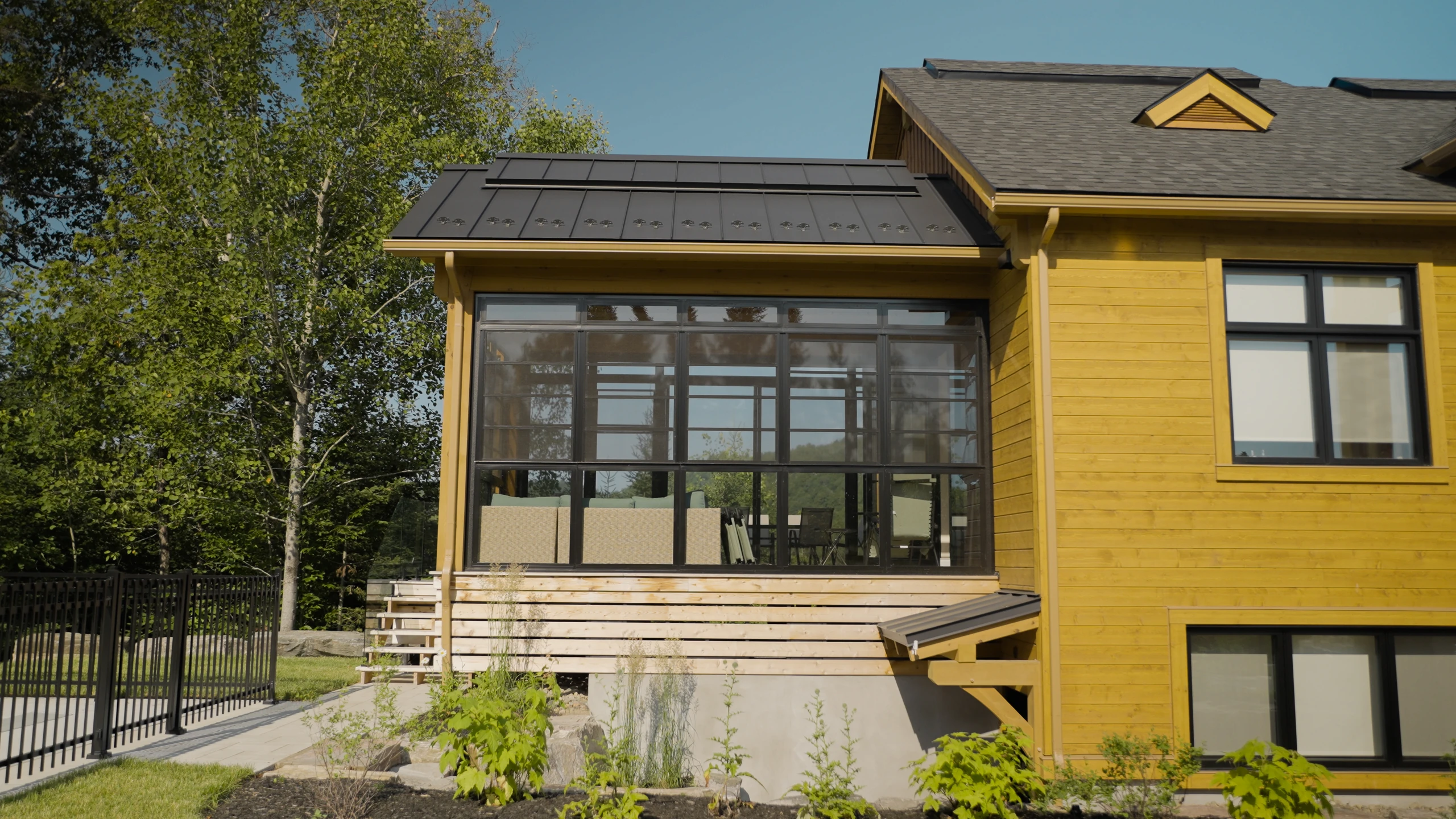 Véranda vitrée et fenêtres sur la façade d’une maison en bois.