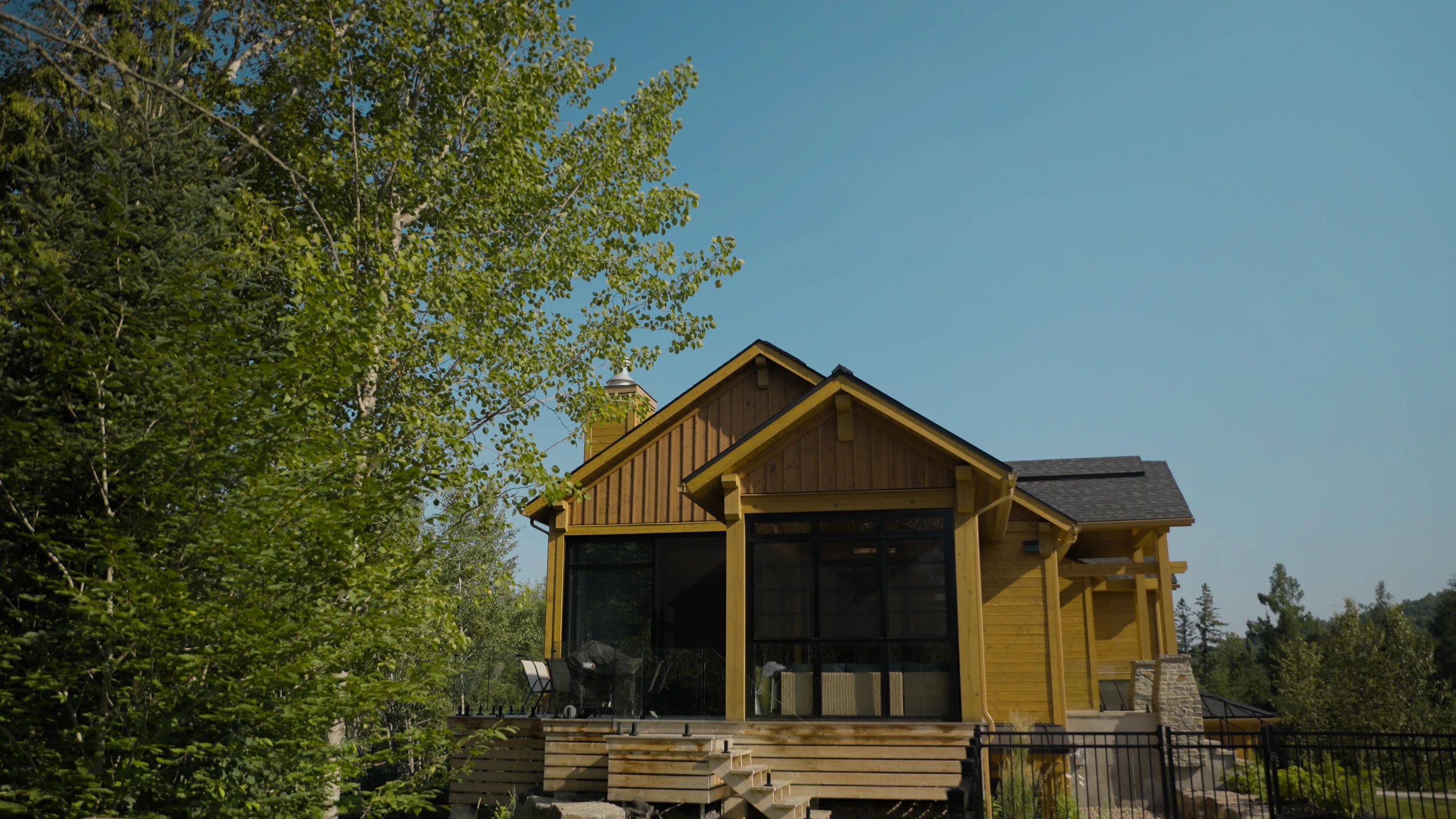 Maison en bois avec véranda vitrée au milieu des arbres.