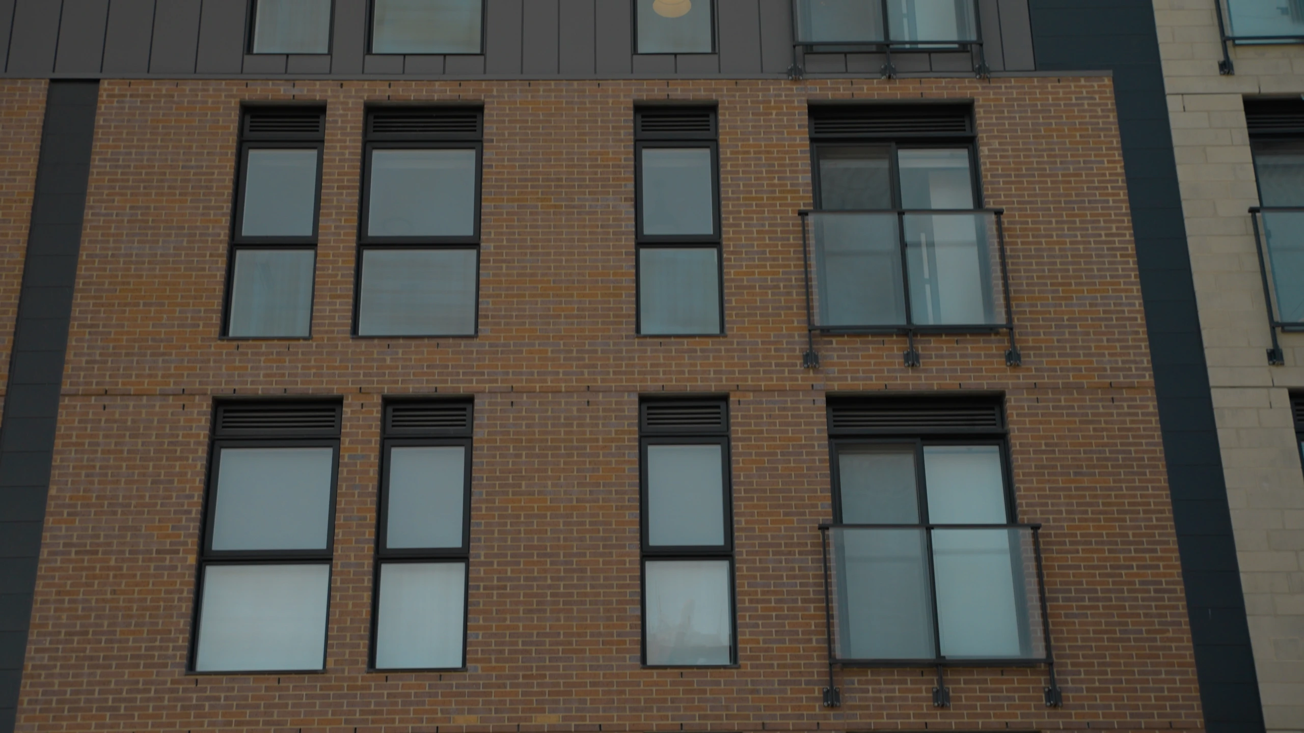 Fenêtres et balcon vitré sur la façade en brique d’un immeuble.